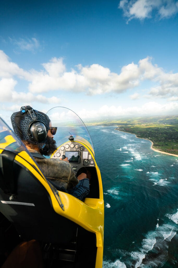 a man in a yellow jet flying over the ocean.