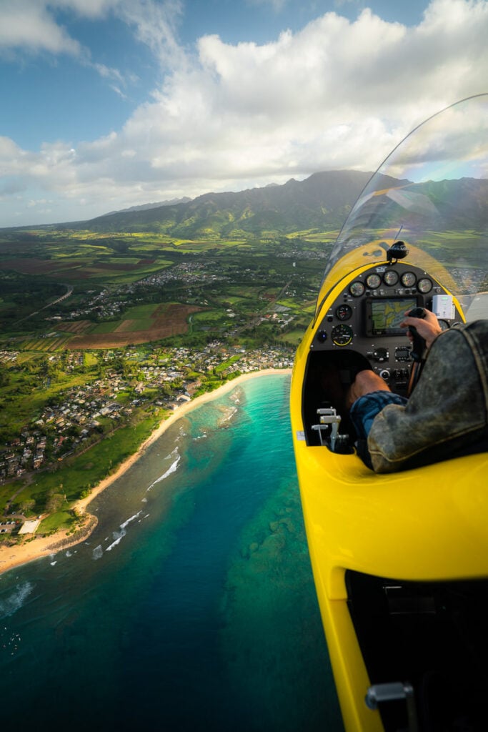 a man flying a plane over a lush green hillside.