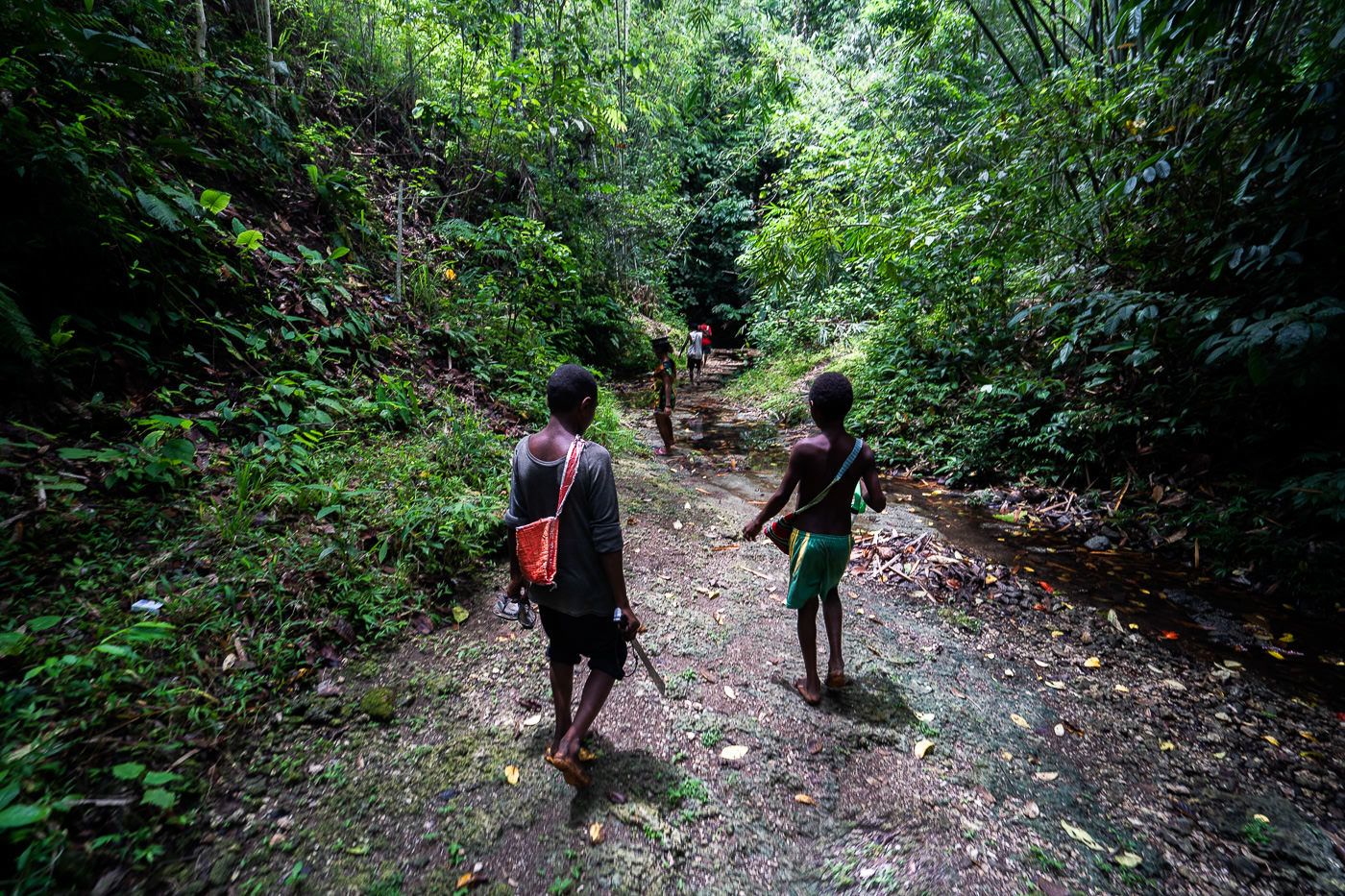 two people walking down a dirt path in the woods.