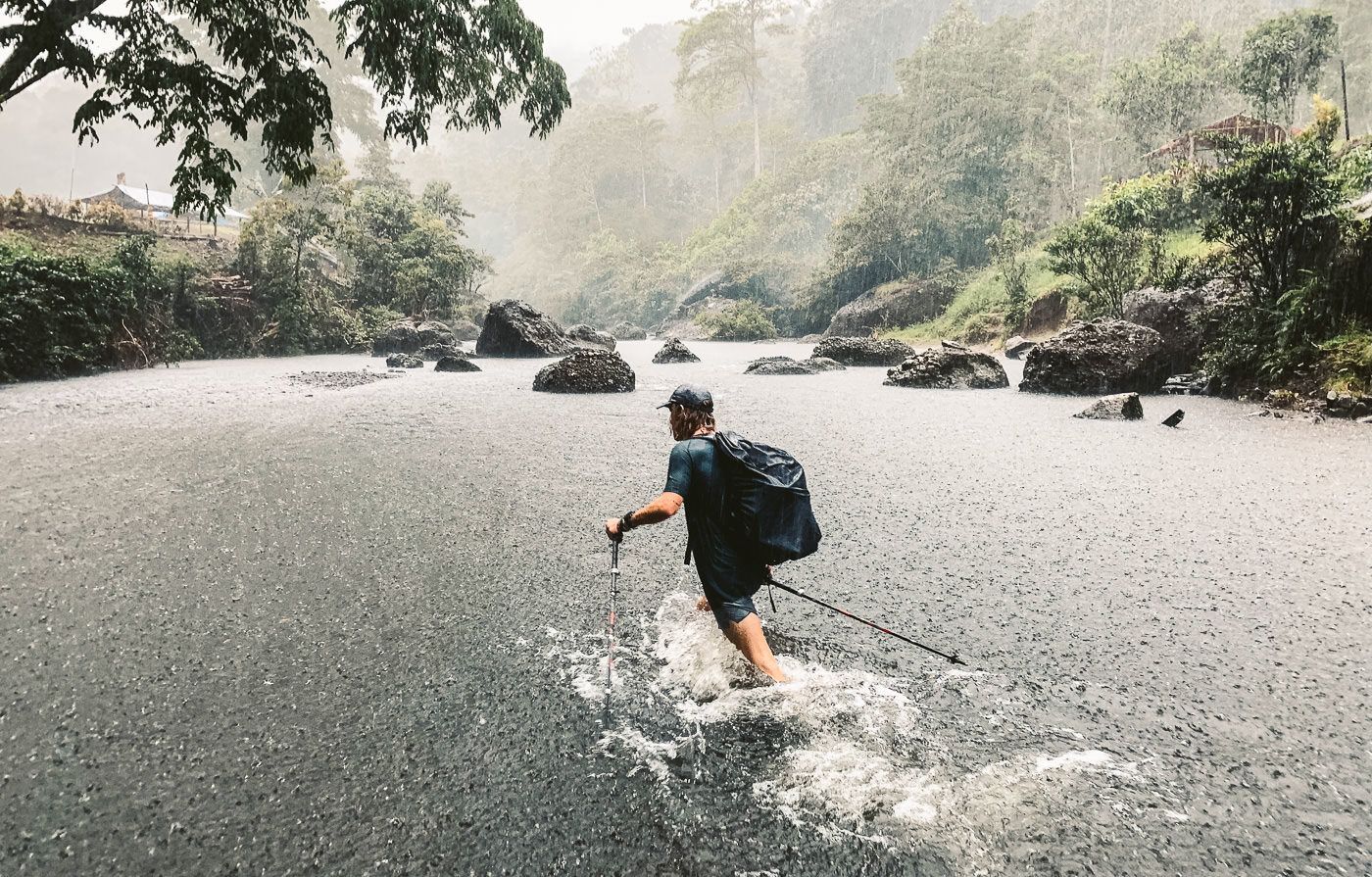 a man walking across a river in the rain.